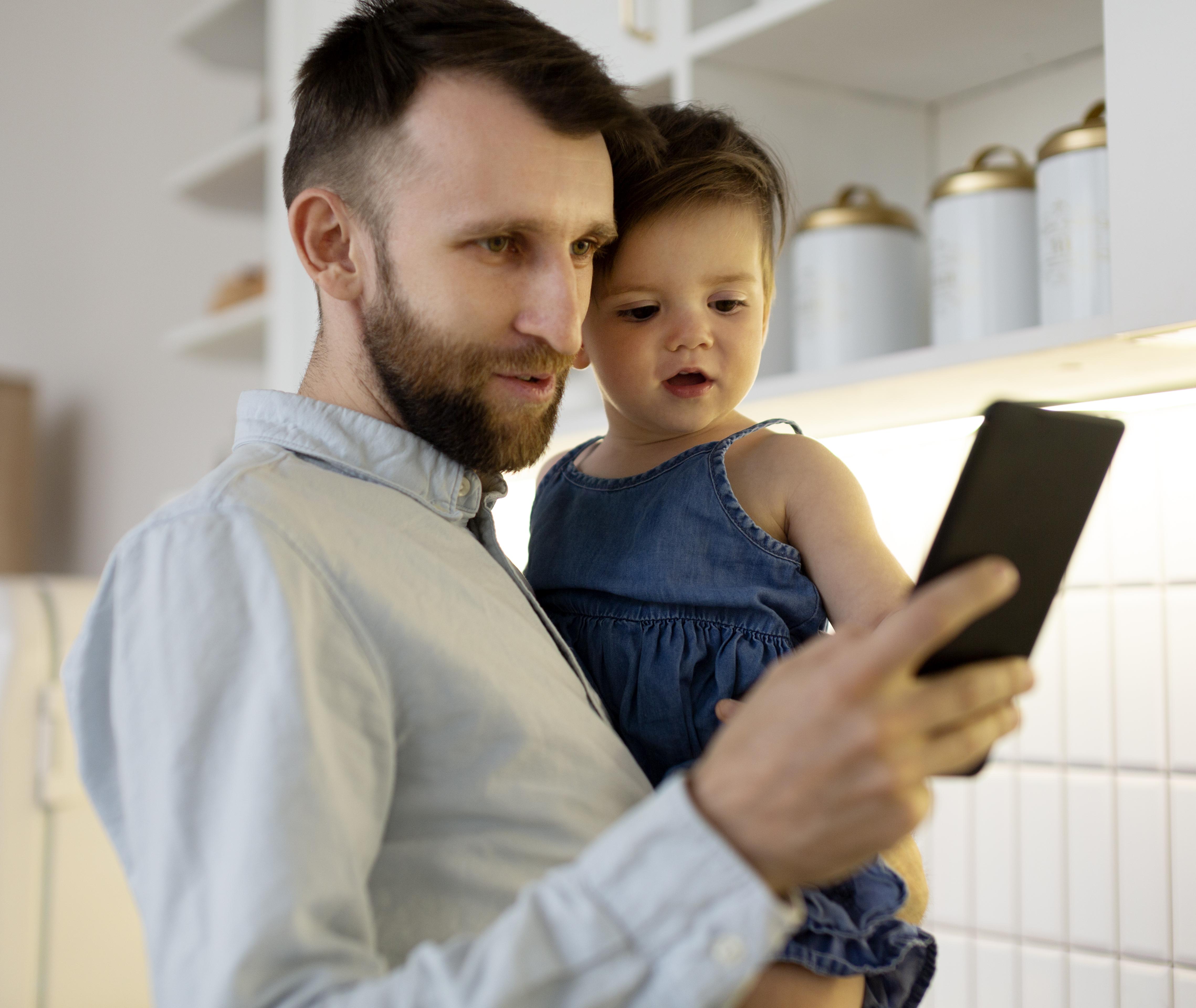 Pai com filha no colo segurando um celular
